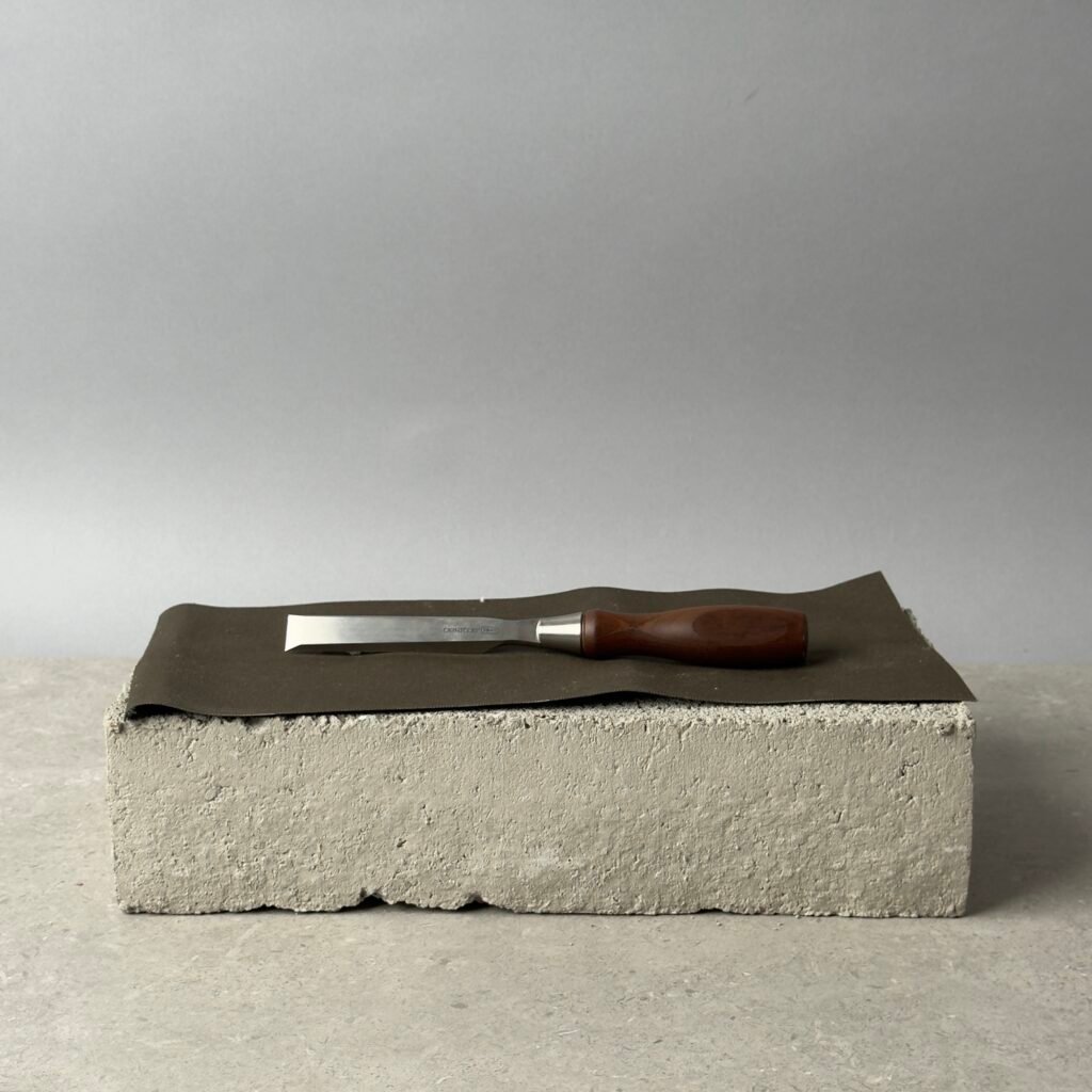 Veritas PM-V11 chisel with wooden handle on a black surface over a concrete block background